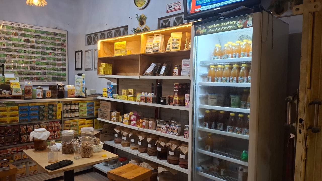 Etalase dan rak produk Pojok Herbal: berbagai kemasan jamu, simplisia dalam toples, dan kulkas berisi botol minuman herbal siap minum